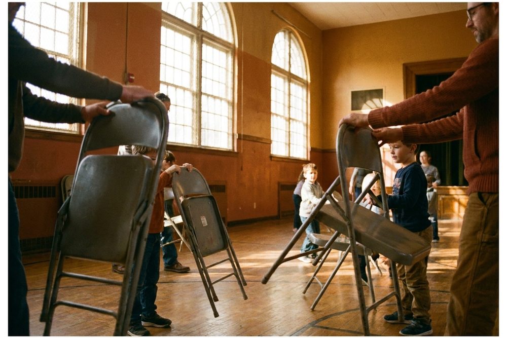 Hands unfolding chairs in a cafetorium, Portra 400 look