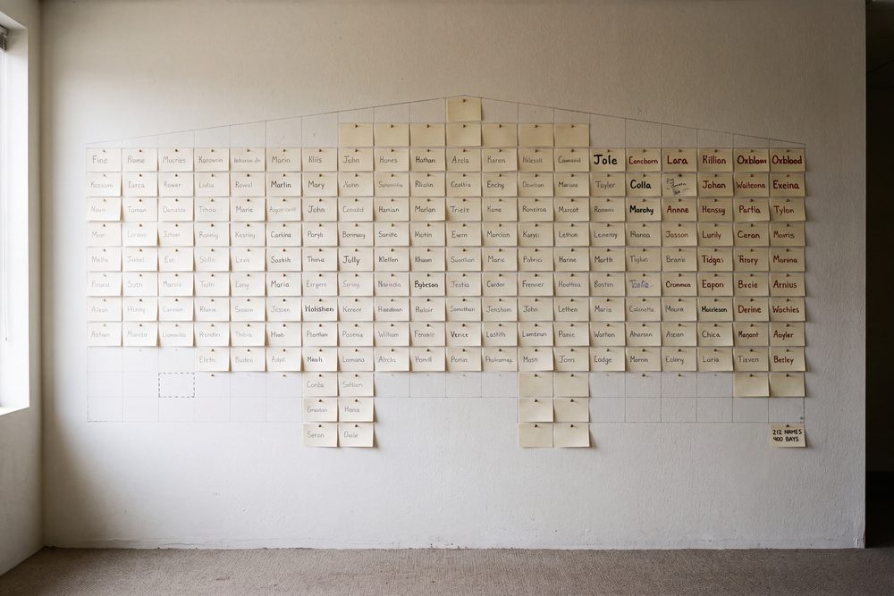 A lobby wall of pinned name cards in the shape of the building